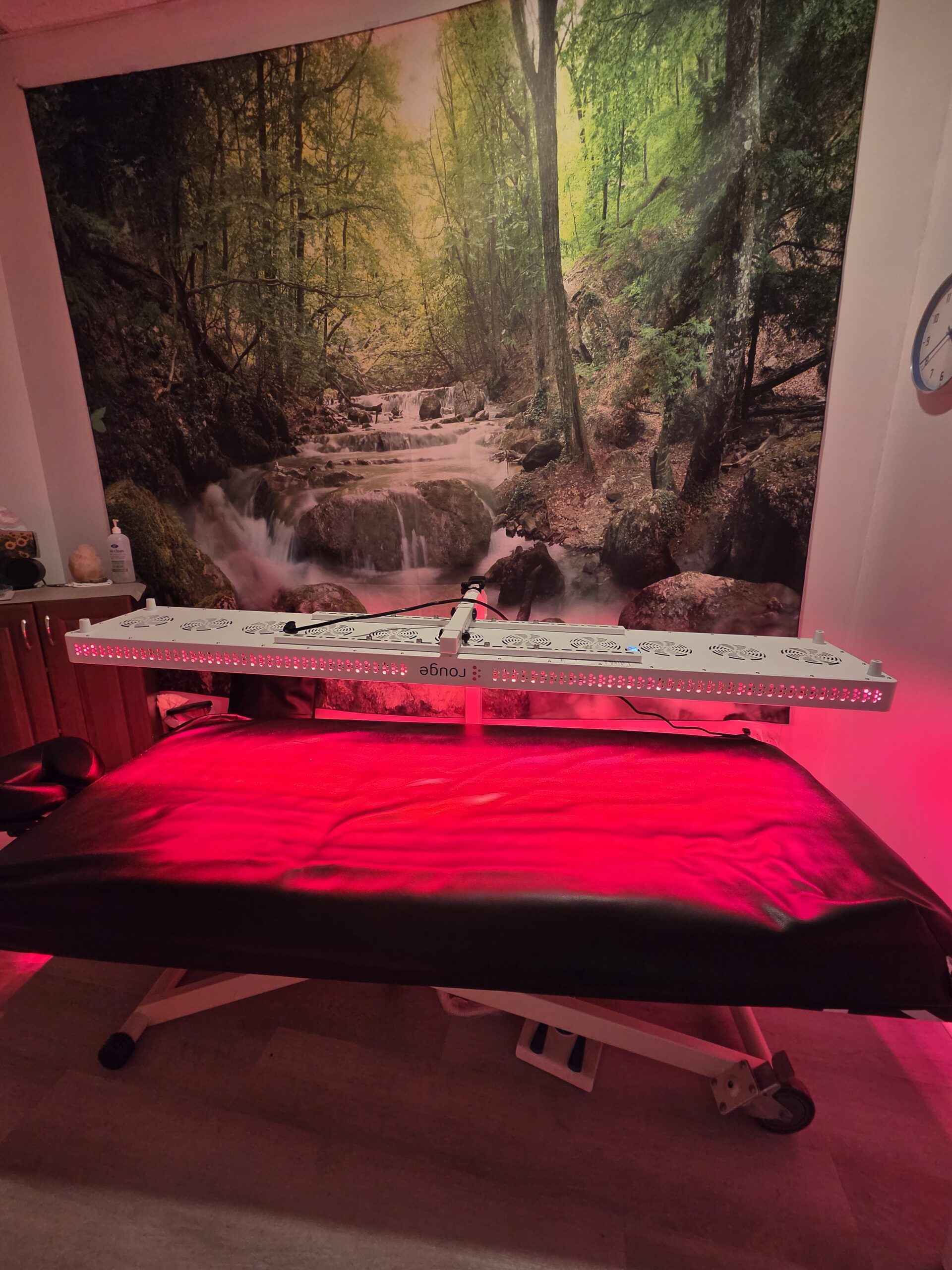 Red light therapy setup: a long LED panel above a massage table with a pillow and towels in a treatment room